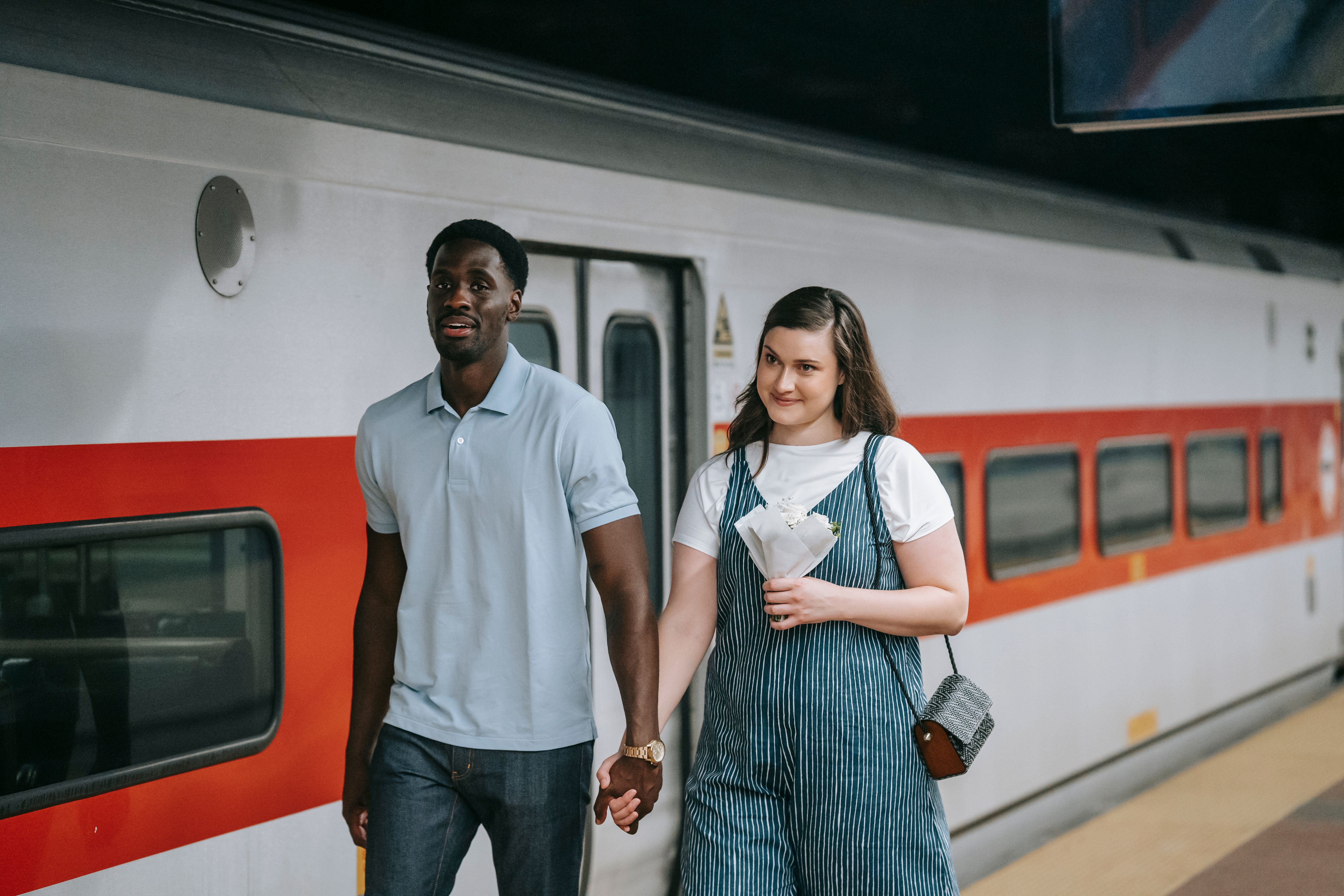 couple%20smiling%20and%20holding%20hands%20while%20walking%20by%20a%20train%20at%20a%20station Couple smiling and holding hands while walking by a train at a station